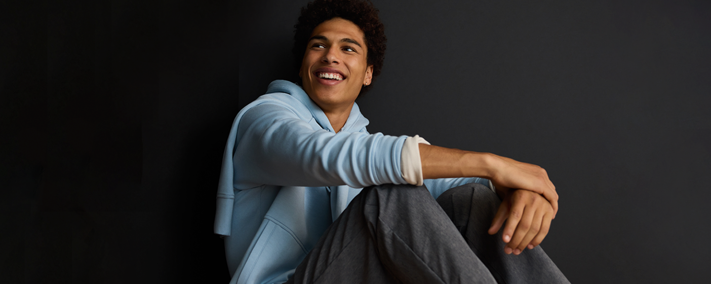 A young black man smiles while sitting on the floor