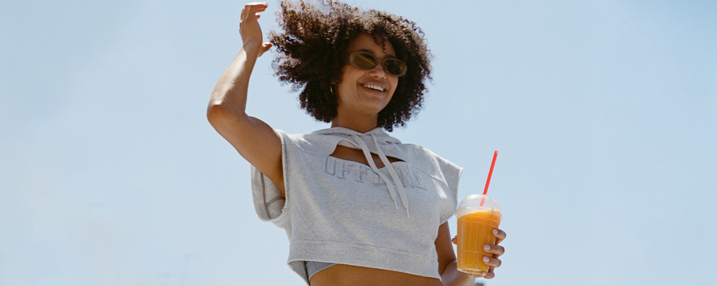 A young bkack woman in sunglasses smiles while holding a fruity drink