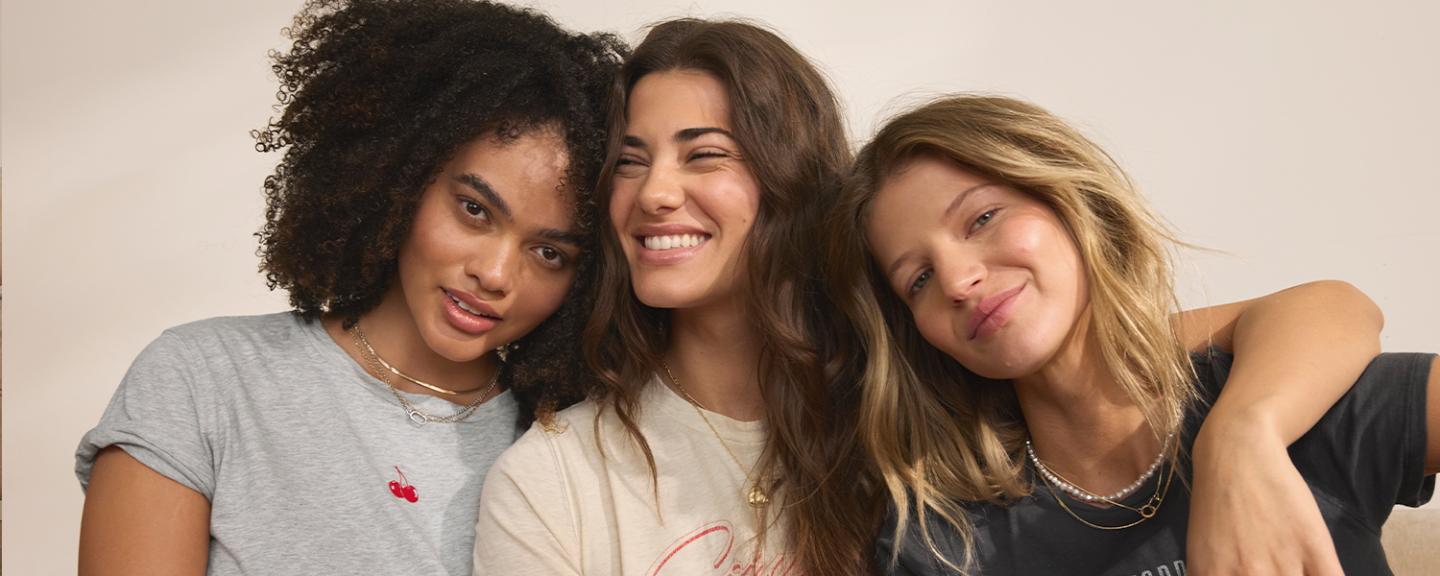 Three young female friends lean on each other, smiling