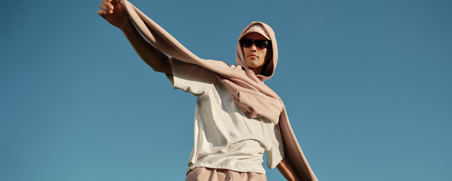 A young man in sunglasses and a hoodie stands outside