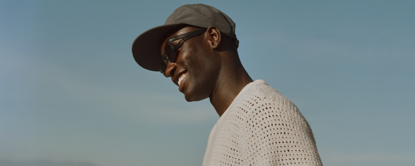 A black man in sunglasses smiles outside