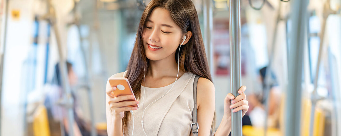 A young asian woman smiles looking at her phone while commuting on the train