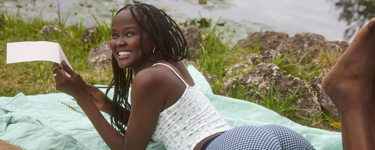 A young black woman smiles while laying on a picnic blanket