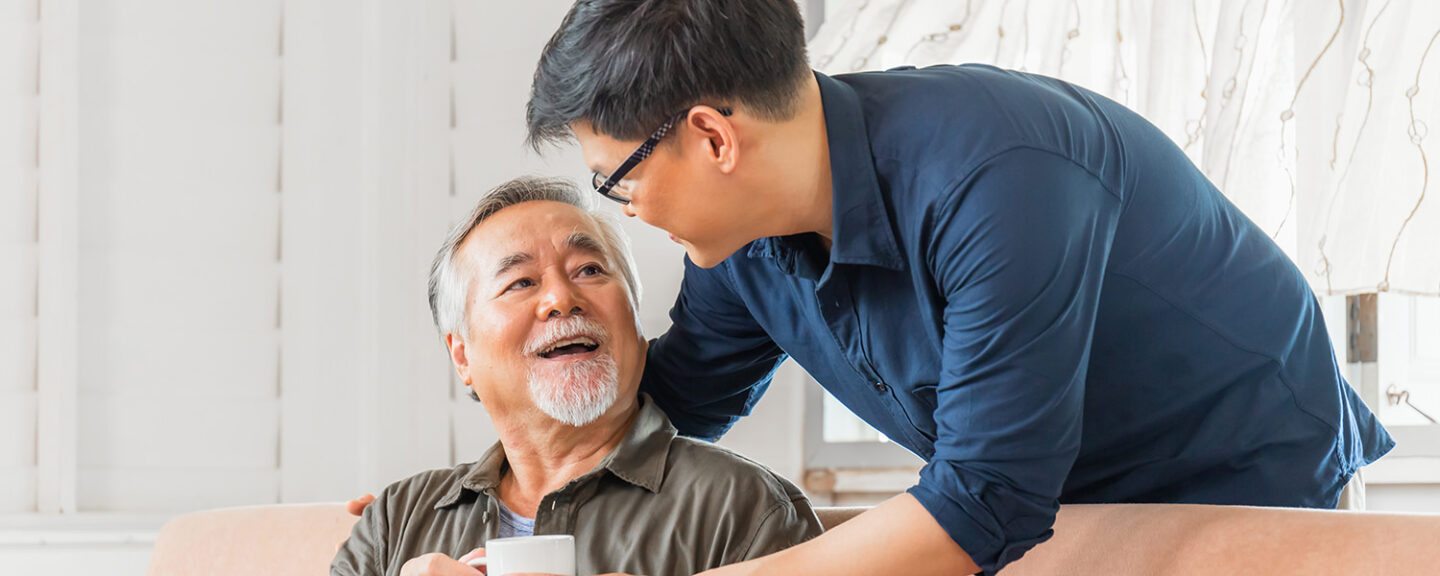 An asian man gives his elderly father a mug of tea
