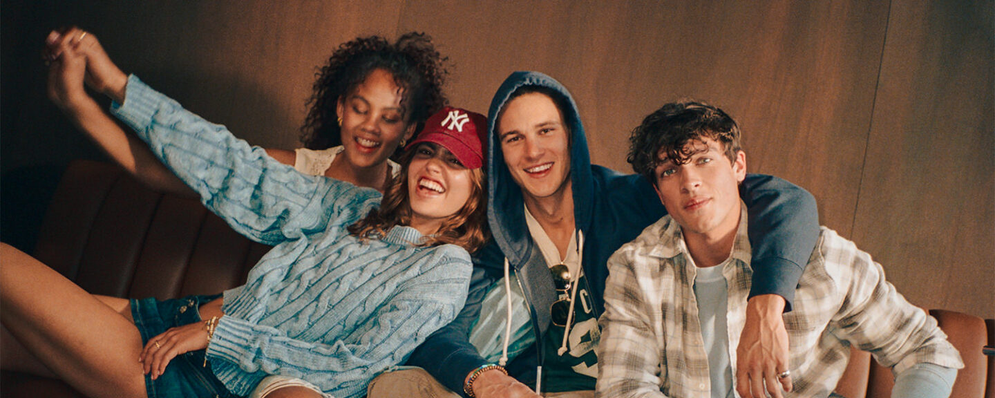 Four young attractive models smile at the camera while sitting on a couch together